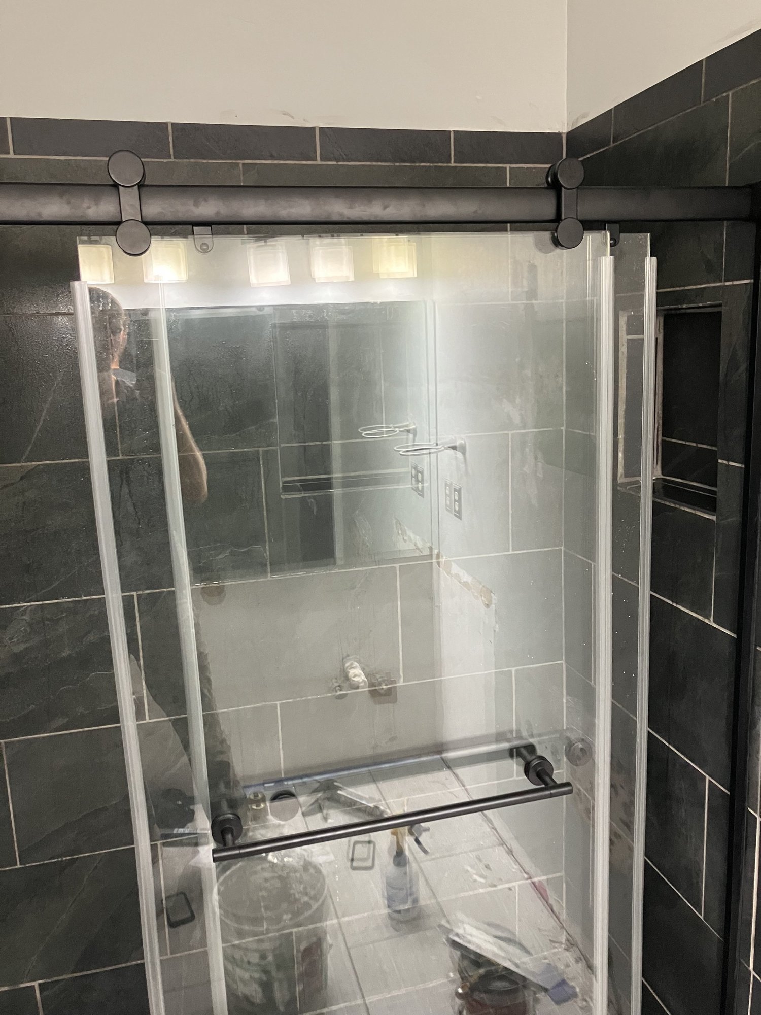 Sliding glass shower door on dark tile during a custom bathroom rehab.